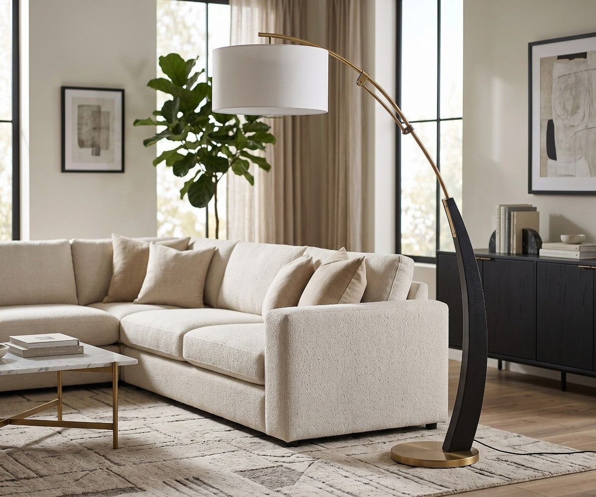 Black and gold arc floor lamp with white drum shade styled beside a sofa in a luxurious, well-lit modern living room