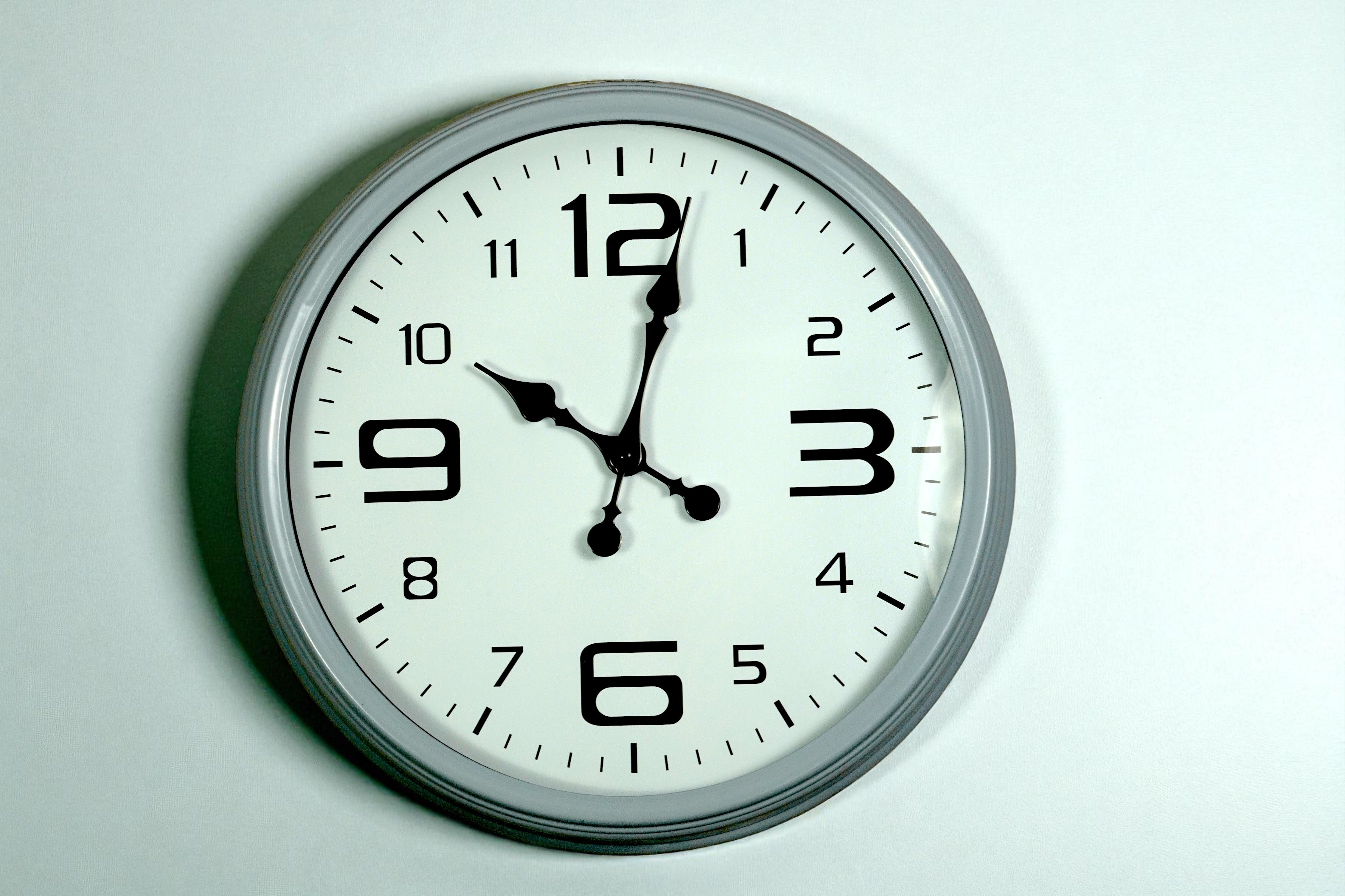 Classic white chrome-rim wall clock with black numerals on a pale wall
