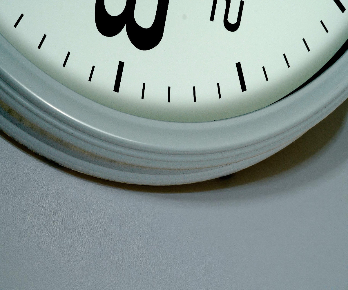 Classic white chrome-rim wall clock with black numerals on a pale wall