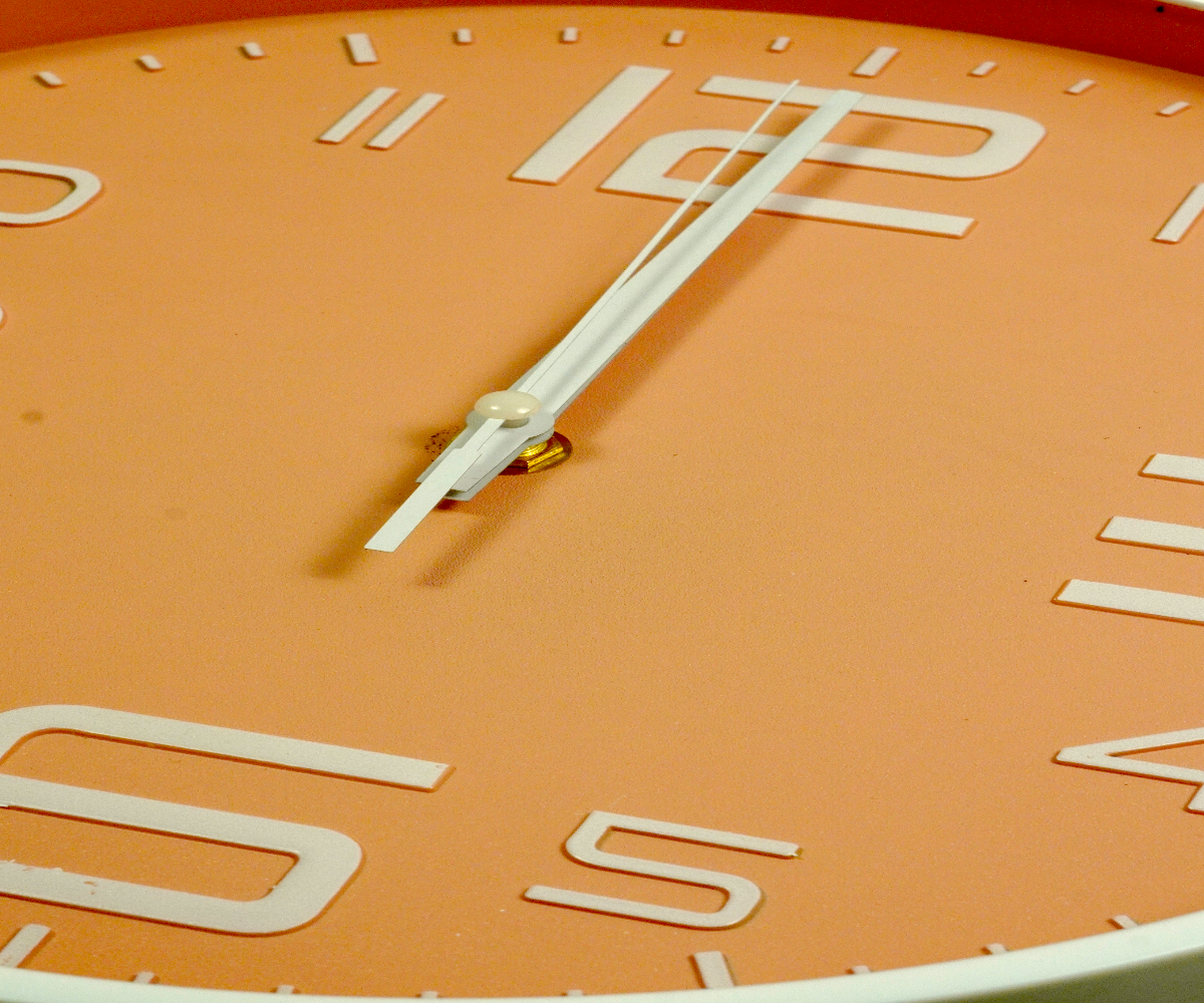 Coral peach minimalist wall clock on rustic wood, surrounded by spring flowers
