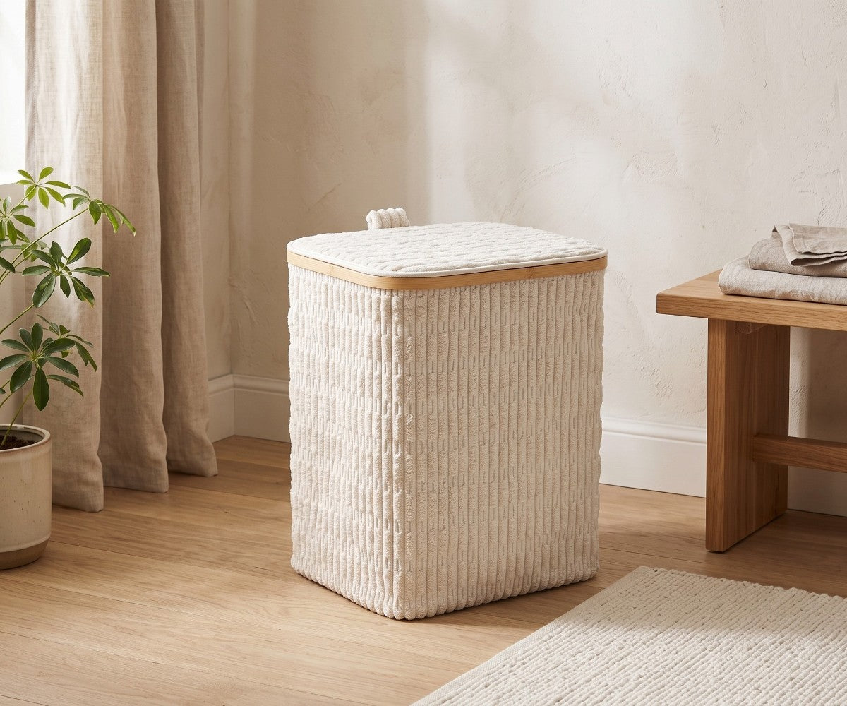 Cream ribbed laundry basket with fitted lid styled in a luxurious, well-lit modern dressing room