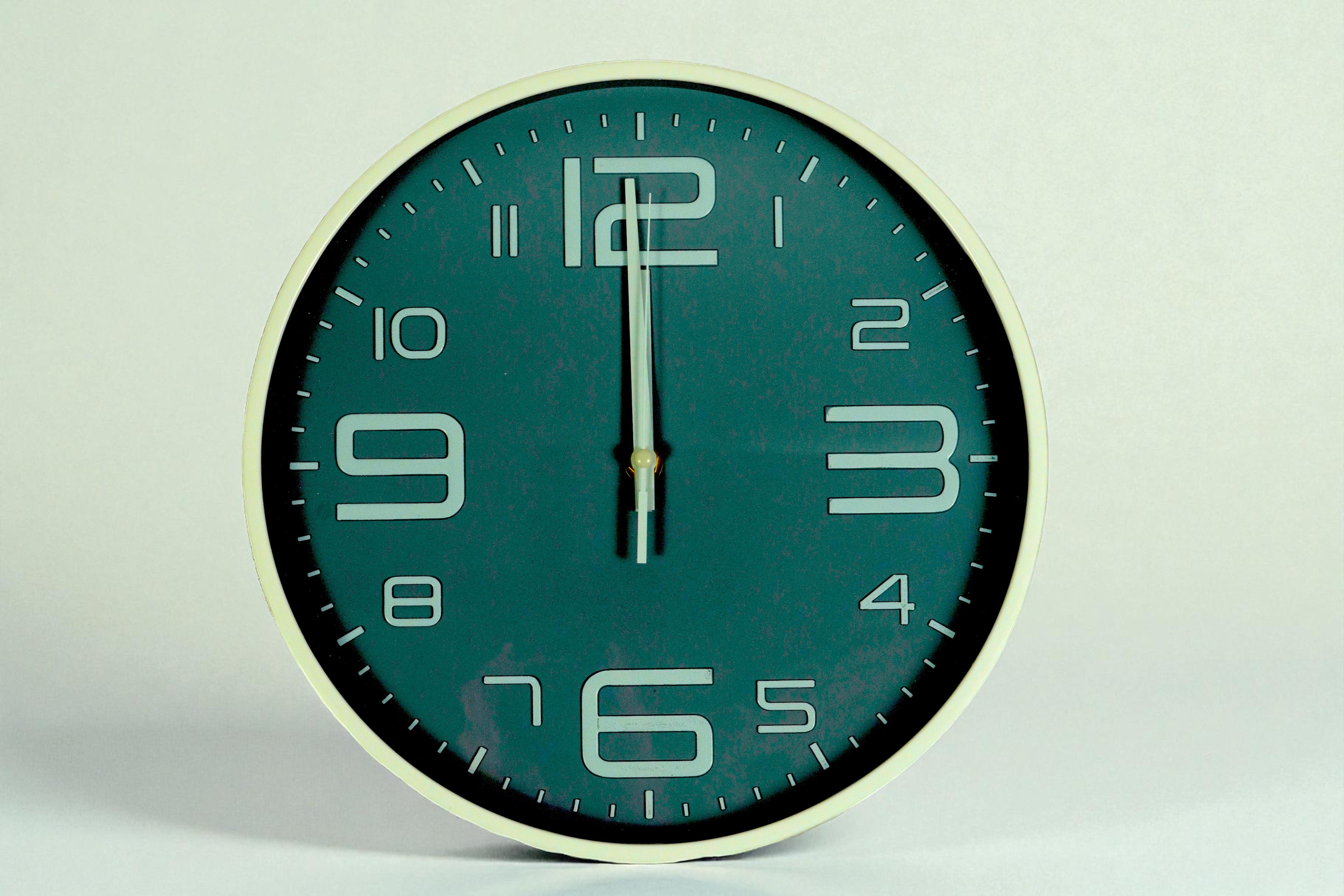 Deep teal outline numeral wall clock with a cream rim on a pale ground