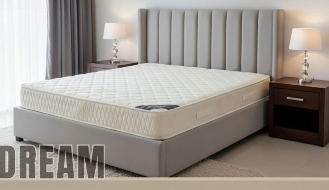 Dream quilted mattress in cream, on a grey bed base beside a dark wood nightstand