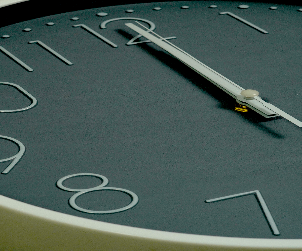 Forest green outline numeral wall clock on a dark wall beside a window