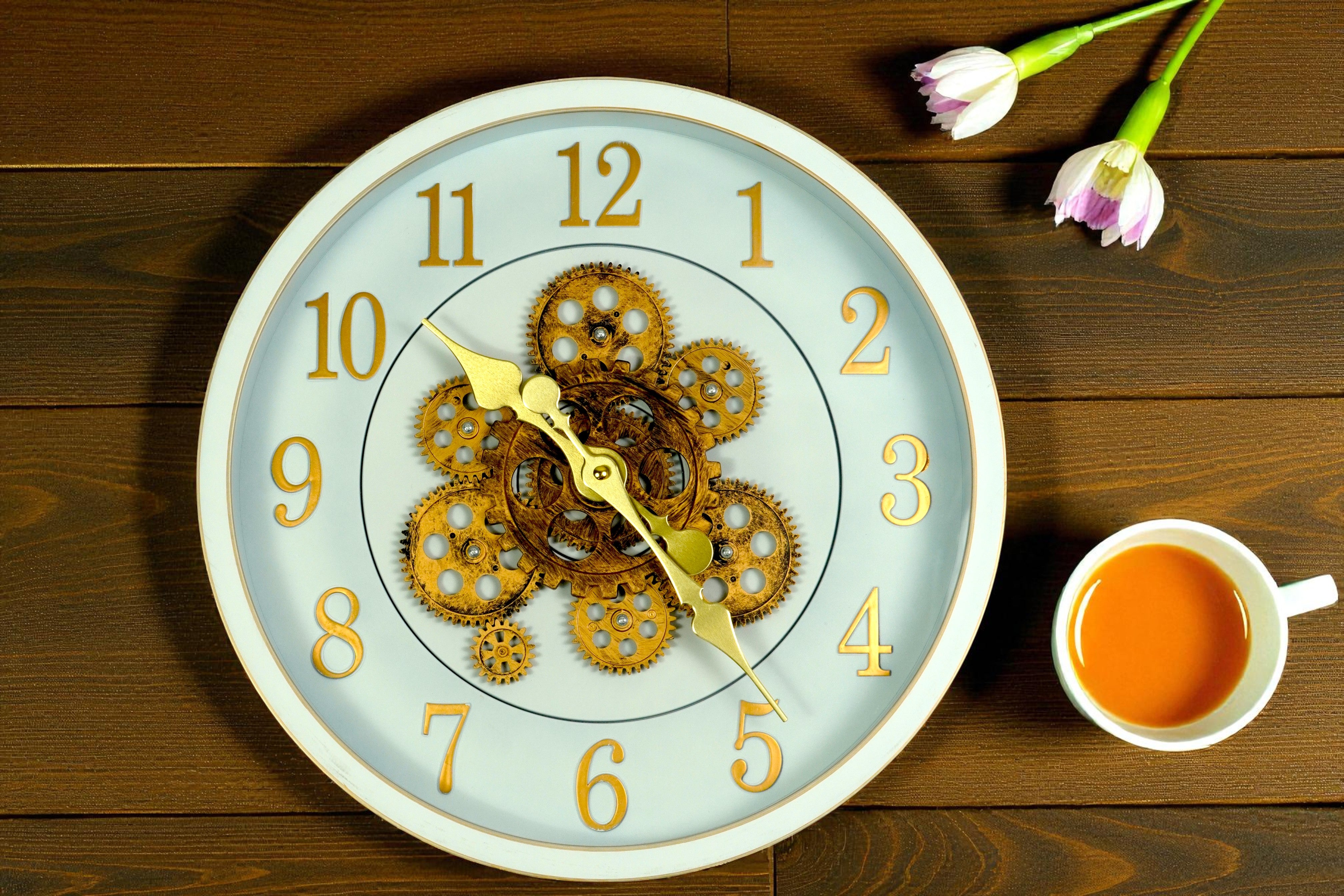 Ivory gold gear skeleton wall clock on wood beside tulips and a cup of tea