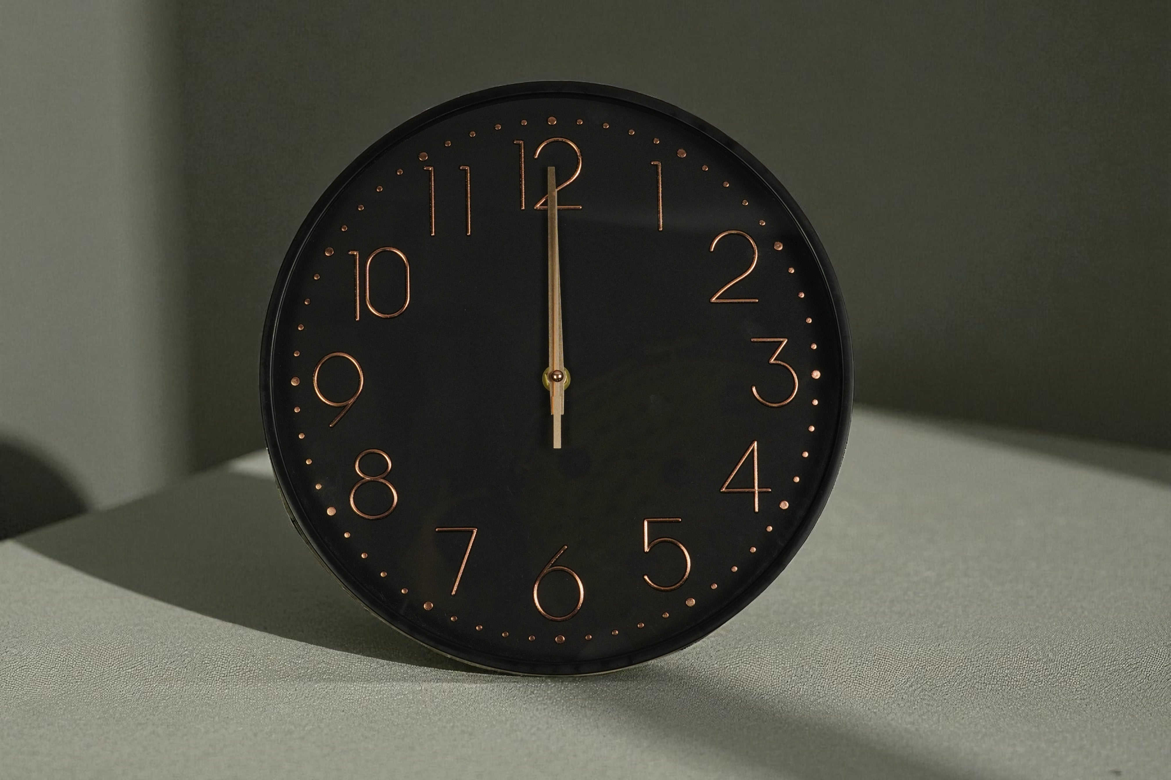 Matte black copper numeral wall clock on a grey surface in raking light