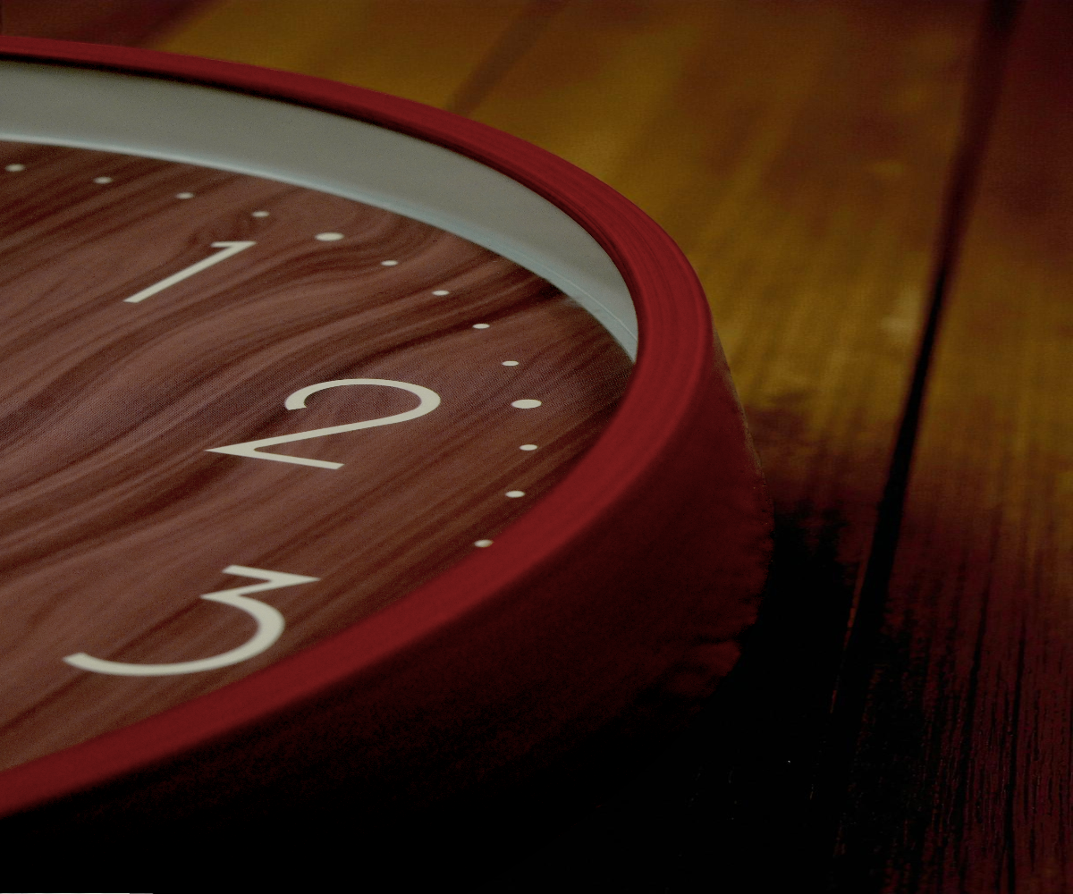 Red rim woodgrain wall clock on a sideboard beside pink tulips