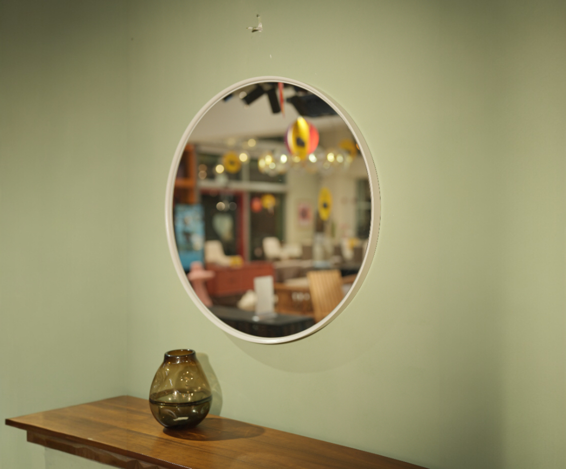 Round modern wall mirror on a sage wall above a walnut console table