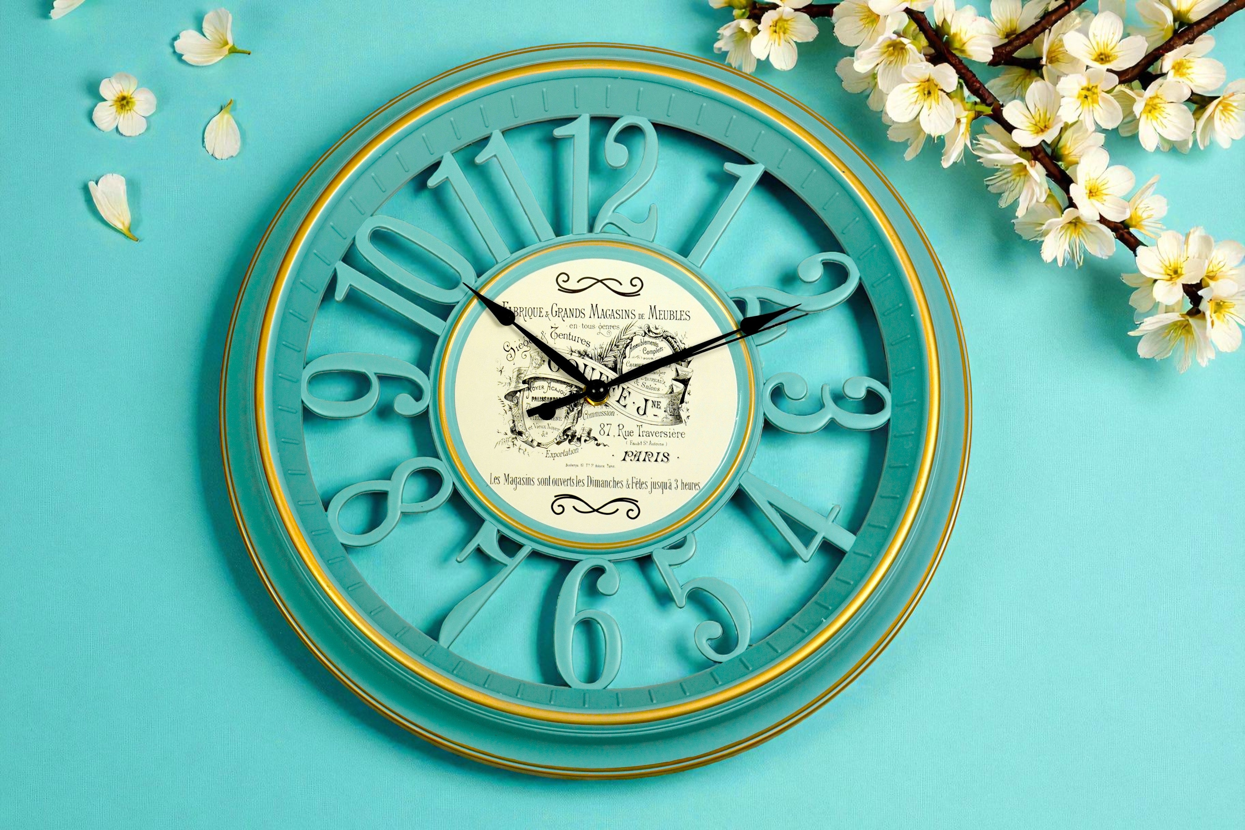 Vintage teal cut-out numeral wall clock with a gold ring, beside blossom