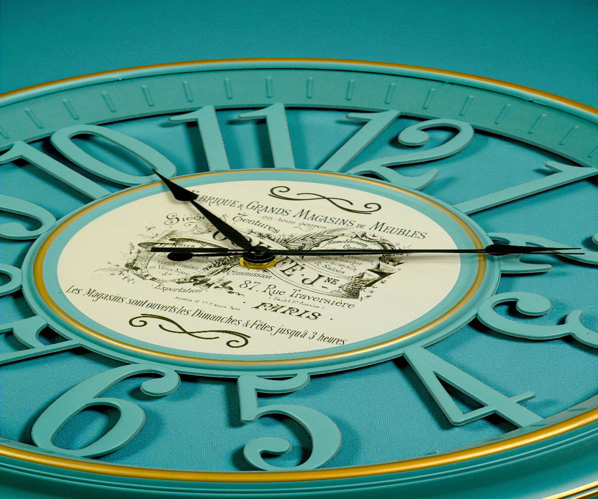 Vintage teal cut-out numeral wall clock with a gold ring, beside blossom