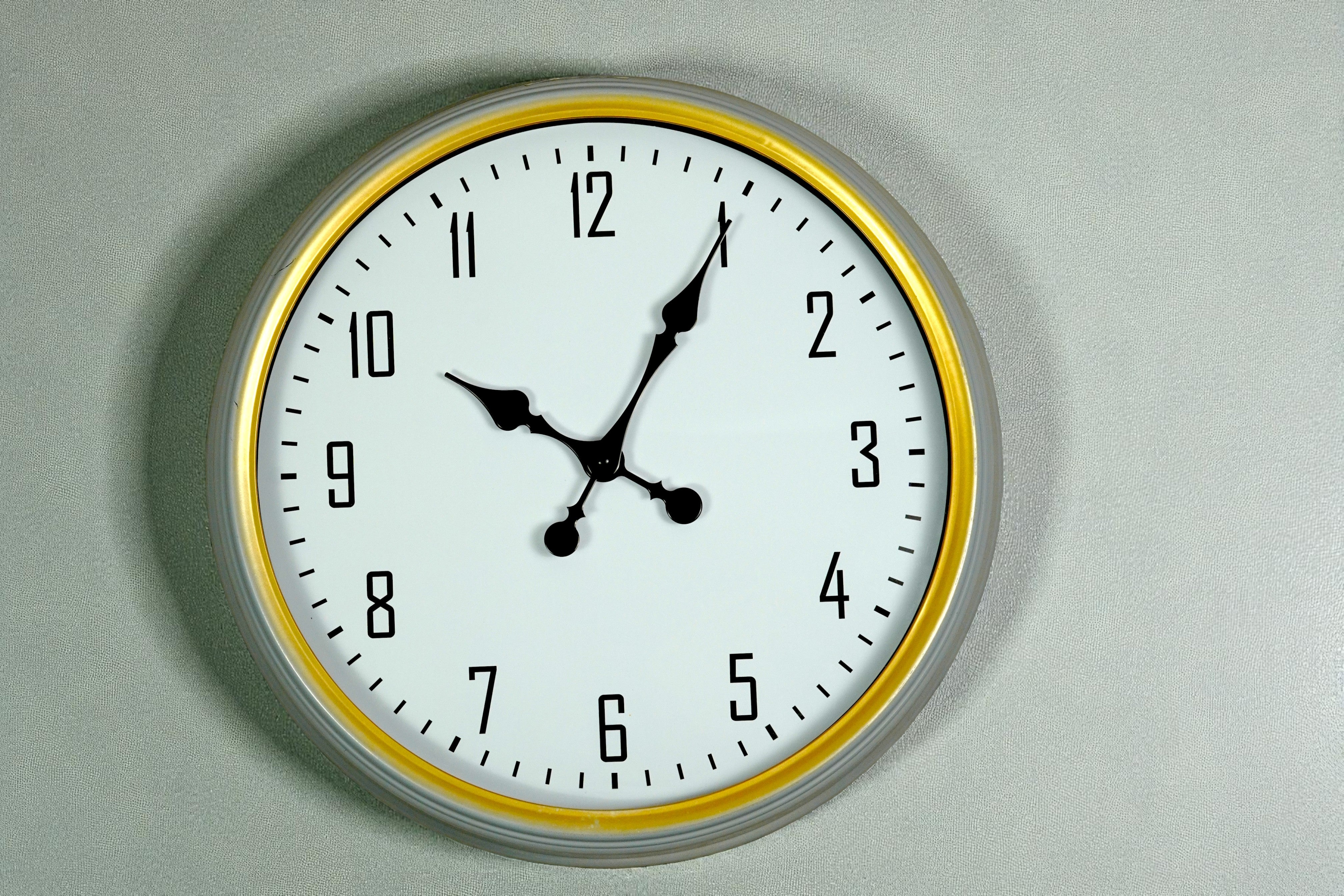 White gold-ring wall clock with black numerals on a grey wall
