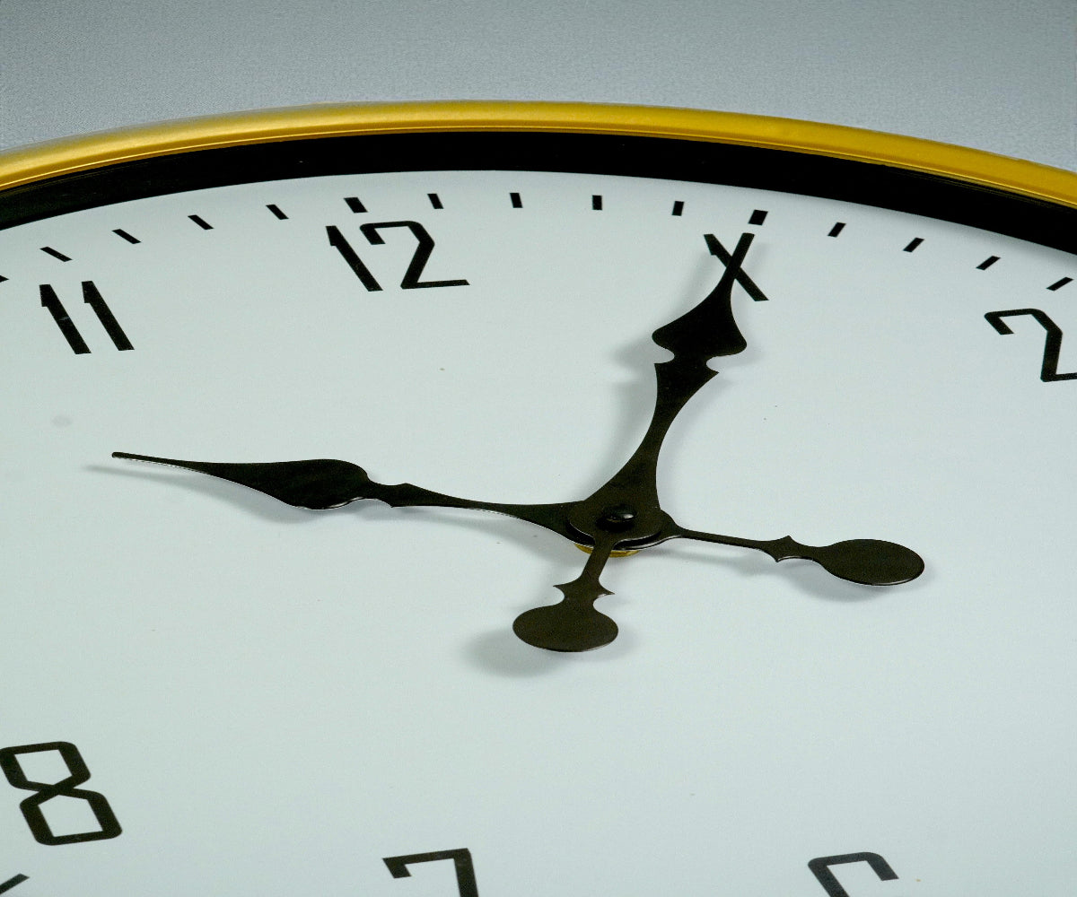 White gold-ring wall clock with black numerals on a grey wall